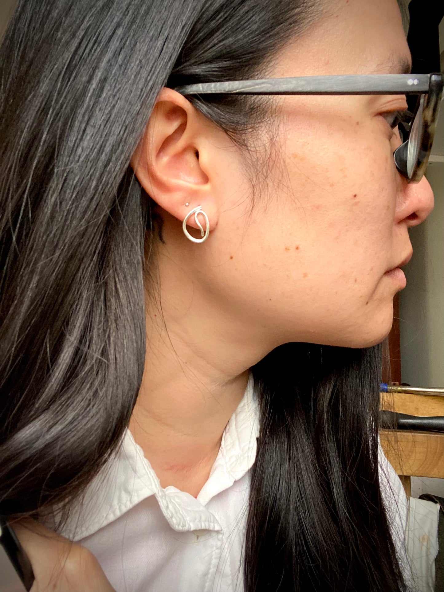 Close-up of unique scribble design stud earrings in sterling silver worn as an earring on a person.