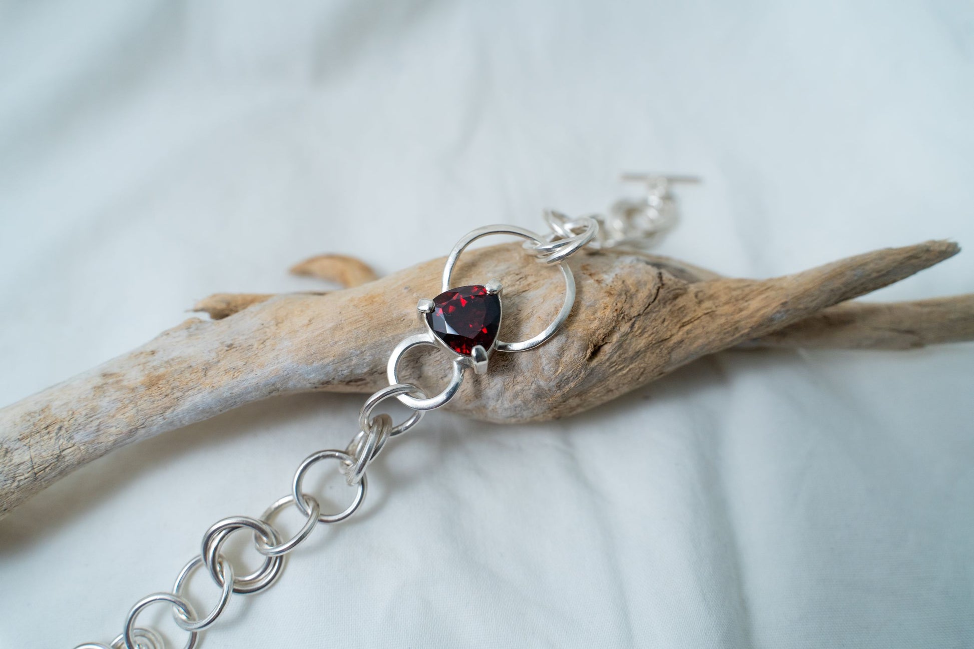 This piece of handcrafted silver bracelet is photographed from a closer point of view to show the magnificence of the trilliant cut garnet. It sits on a piece of driftwood found in Hong Kong.