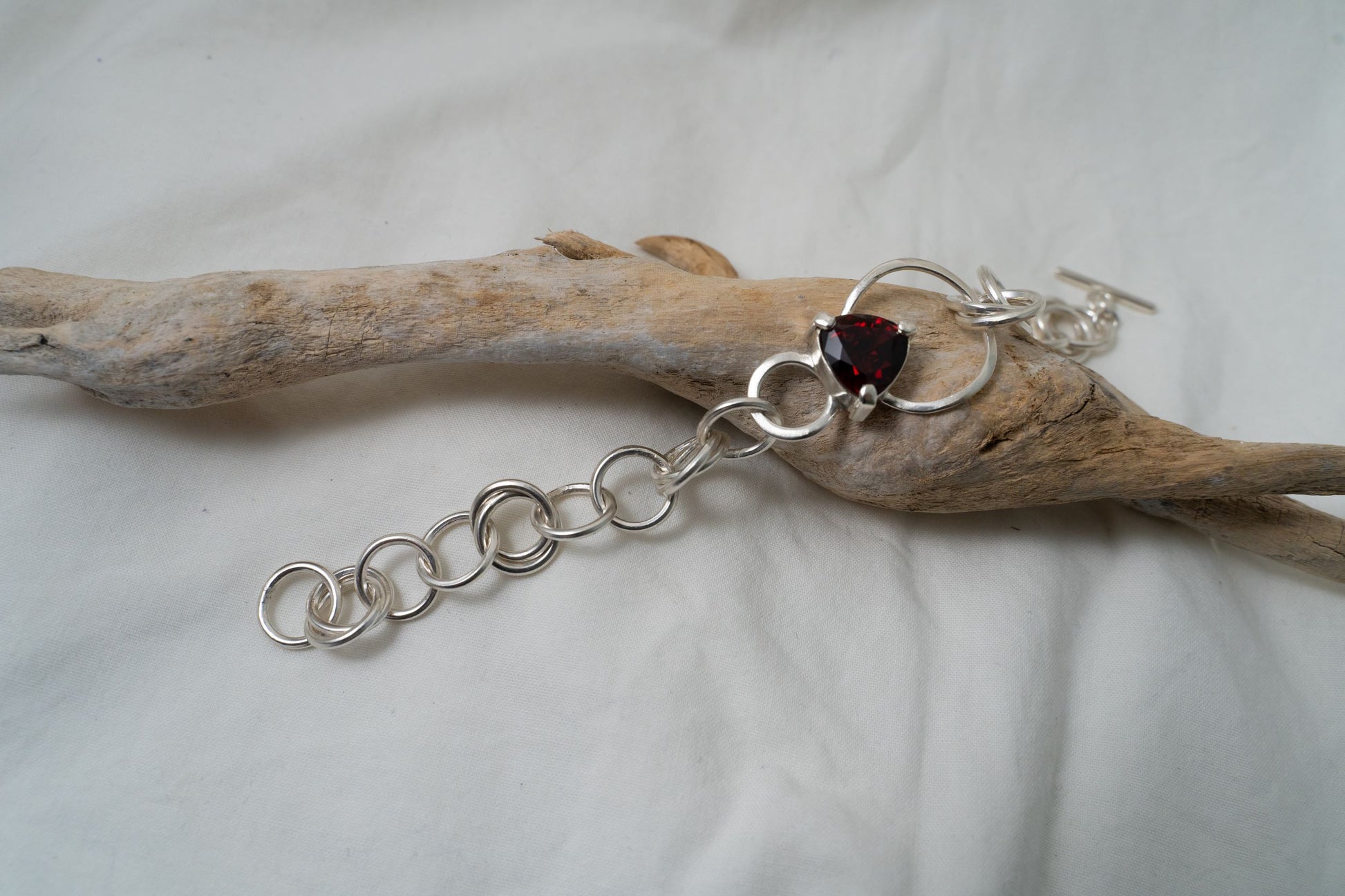 This piece of handcrafted silver bracelet is photographed from a closer point of view to show the magnificence of the trilliant cut garnet. It sits on a piece of driftwood found in Hong Kong.
