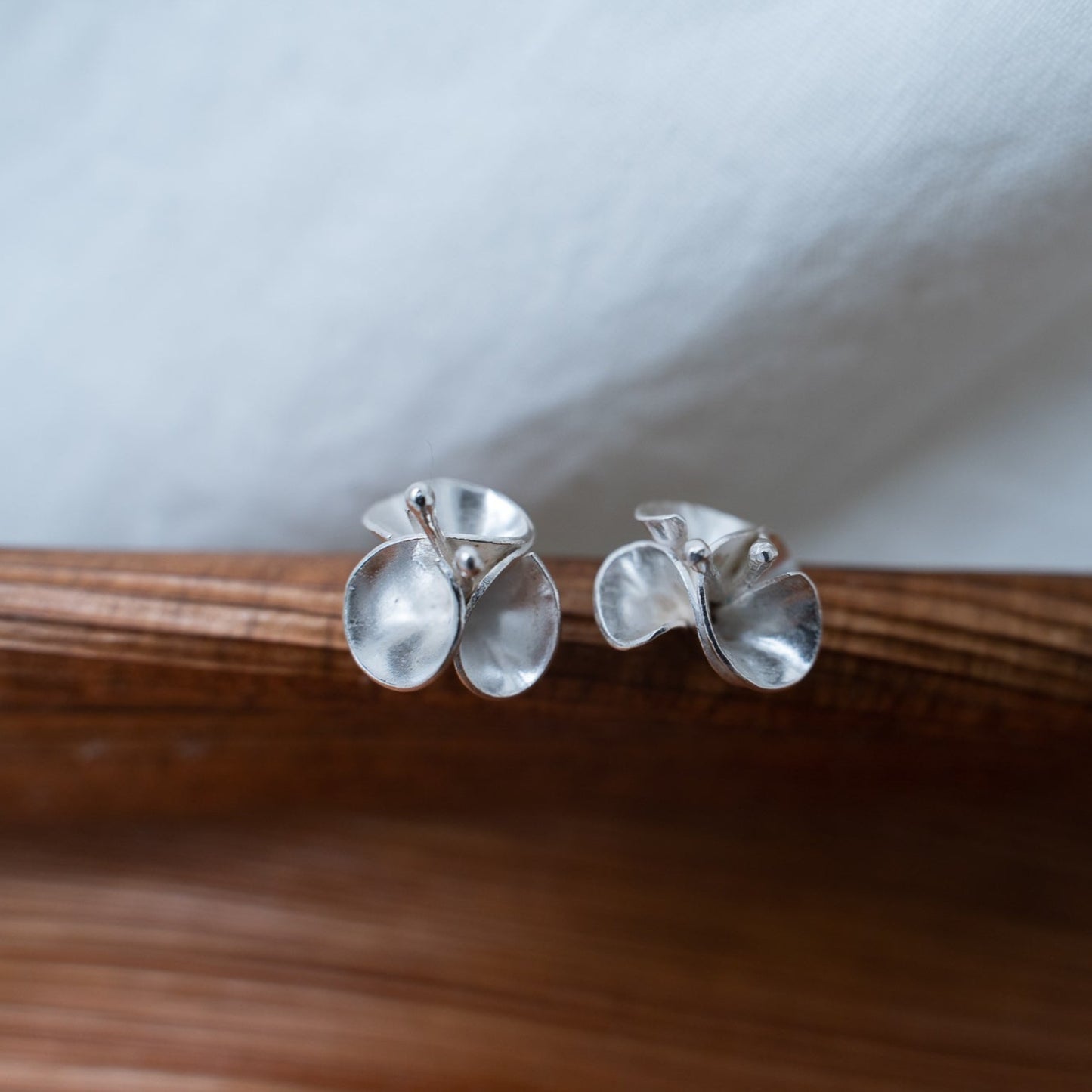 handcrafted floral silver studs photographed on a piece of driftwood. These studs are designed after the bourgainvillea flowers from Southern Africa. A flower that reminds me of home, these delicate pieces are meant to sit delicately on your ear.
