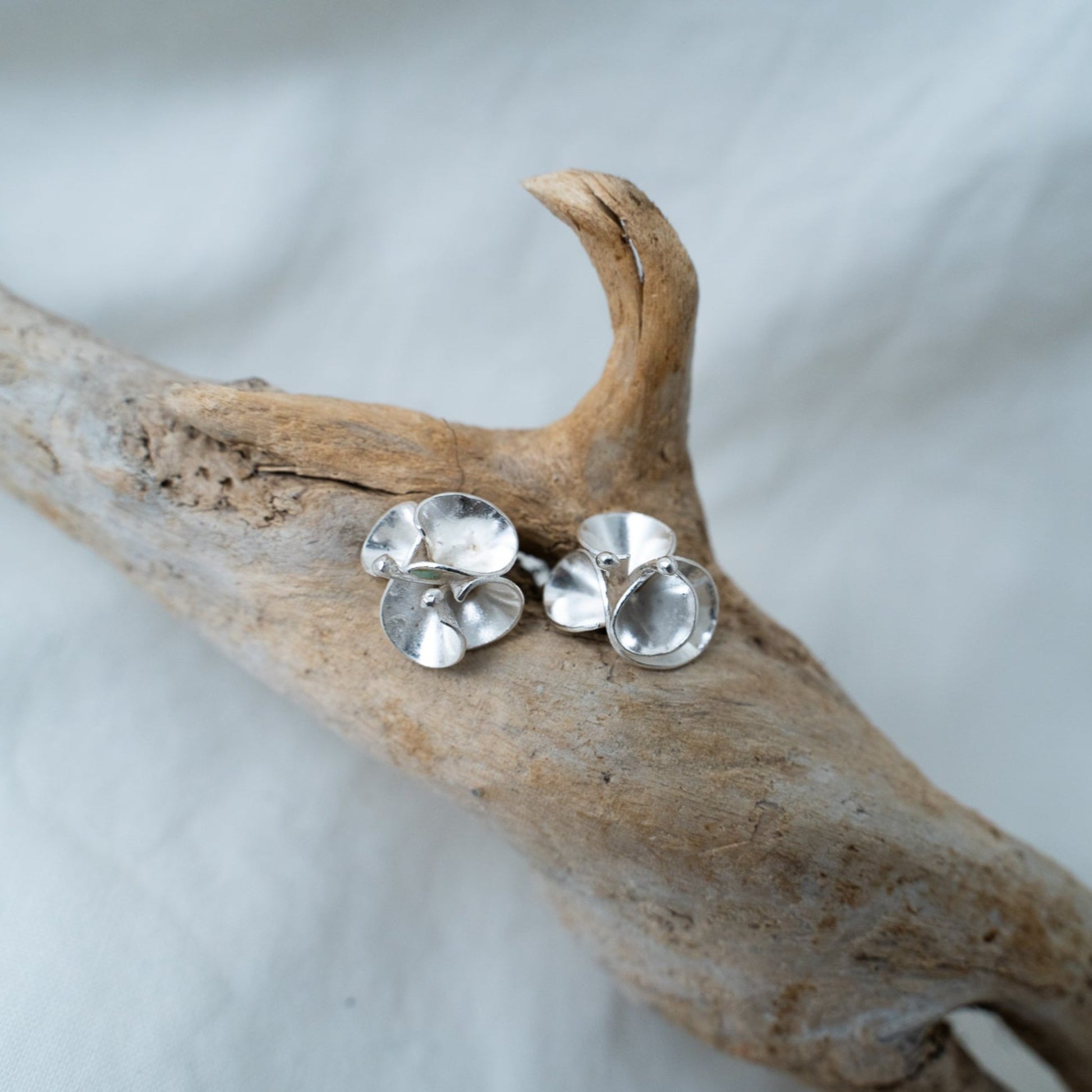 handcrafted floral silver studs I named Branka are photographed on a piece of driftwood. These studs are designed after the bourgainvillea flowers from Southern Africa. A flower that reminds me of home, these delicate pieces are meant to sit delicately on your ear.