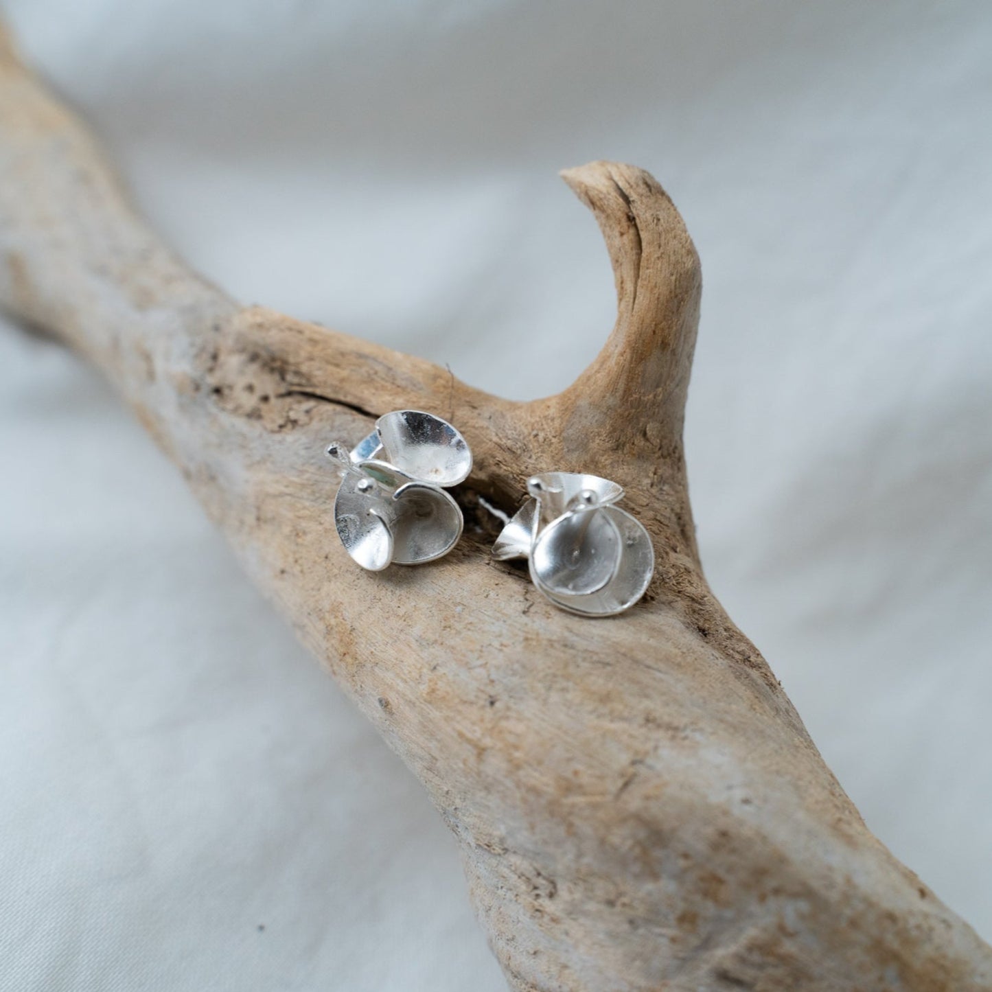 handcrafted floral silver studs I named Branka are photographed on a piece of driftwood. These studs are designed after the bourgainvillea flowers from Southern Africa. A flower that reminds me of home, these delicate pieces are meant to sit delicately on your ear showing the curves of the petals and the lovely stigmas of the flower.