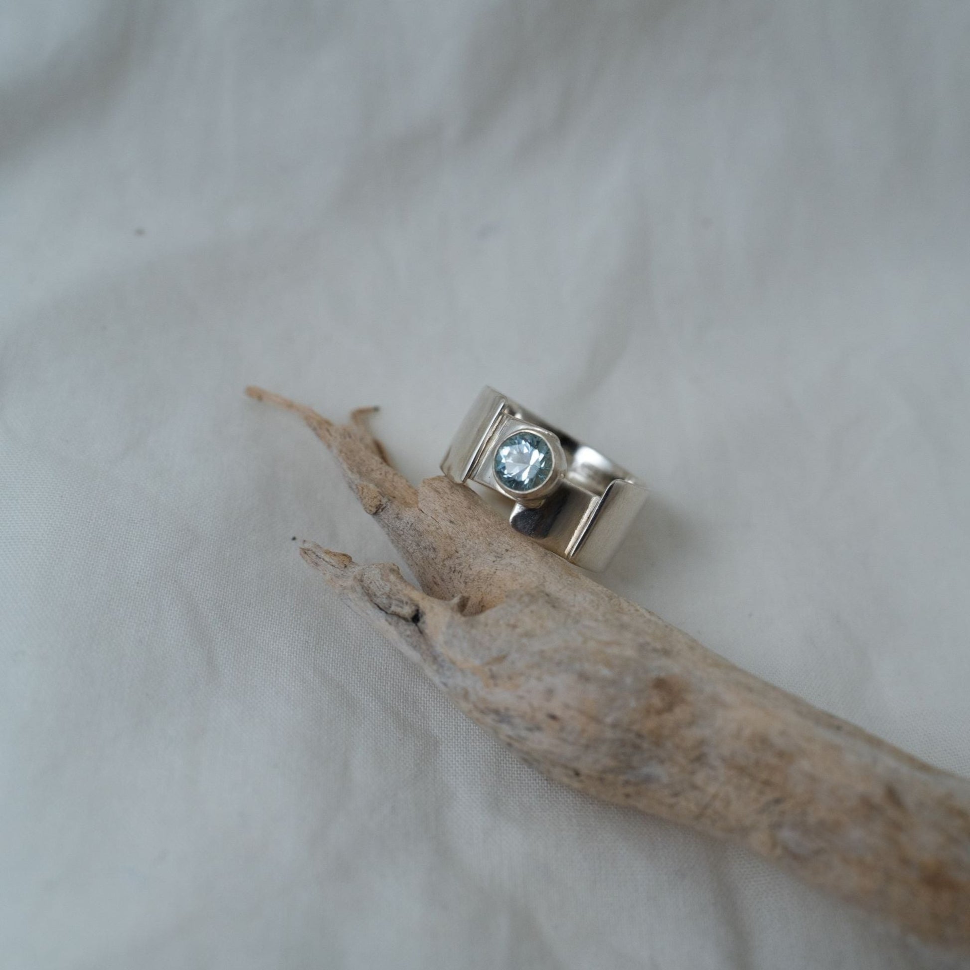 A look at the round cut, aquamarine that is bezel set in the center of the gender-fluid, chunky silver ring.