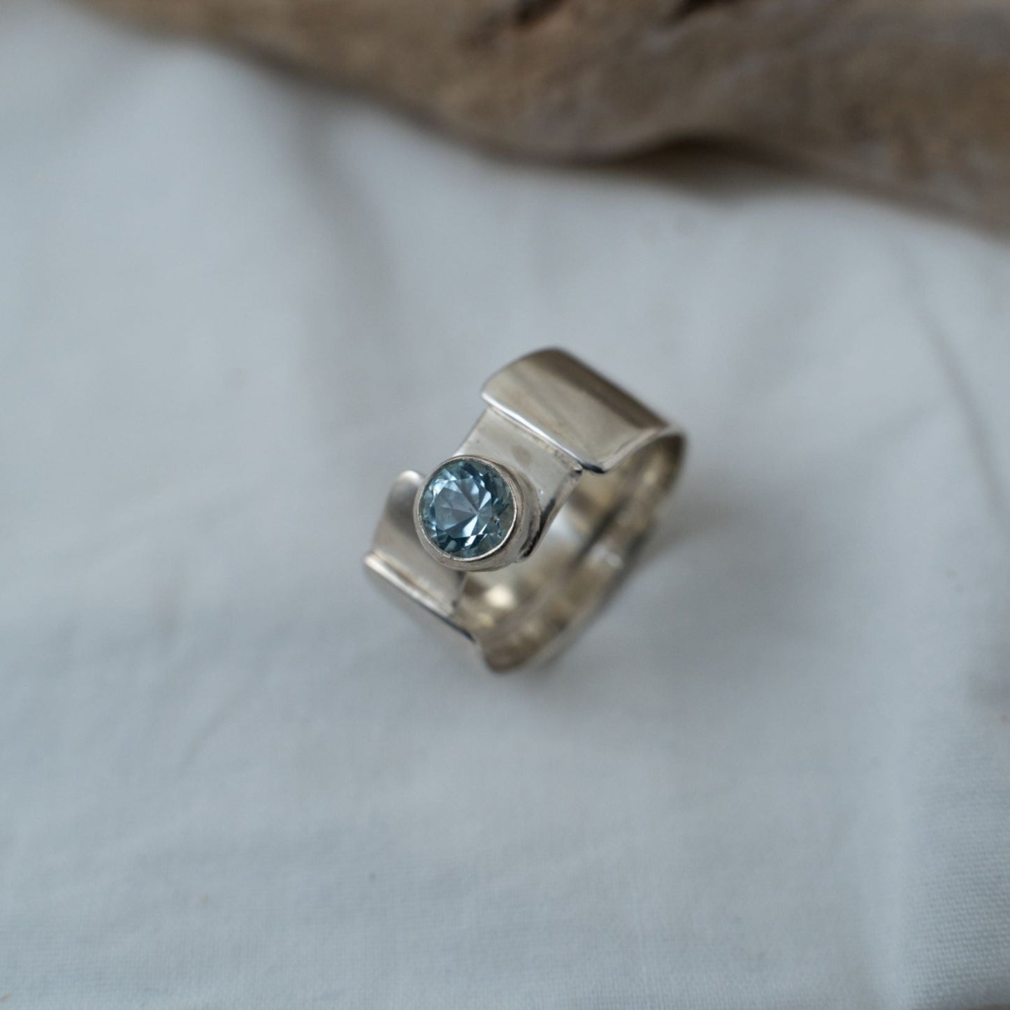A closer look taken of the round cut aquamarine that is bezel set in this gender fluid silver ring. It shows the true color and different facets you can see with the ring.