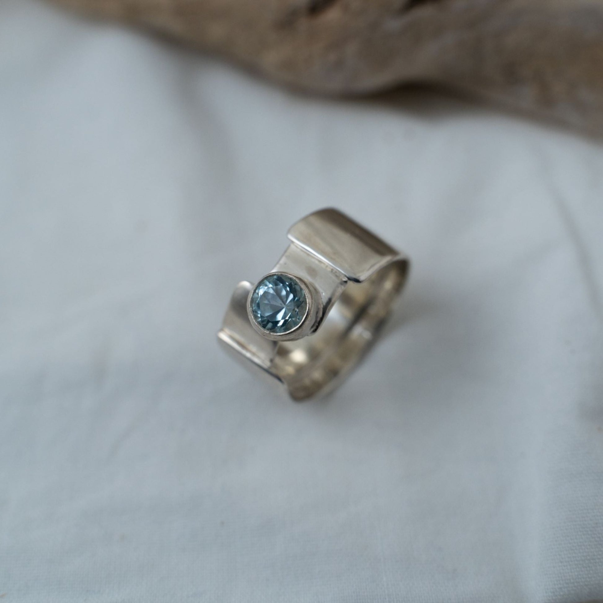 A closer look taken of the round cut aquamarine that is bezel set in this gender fluid silver ring. It shows the true color and different facets you can see with the ring.
