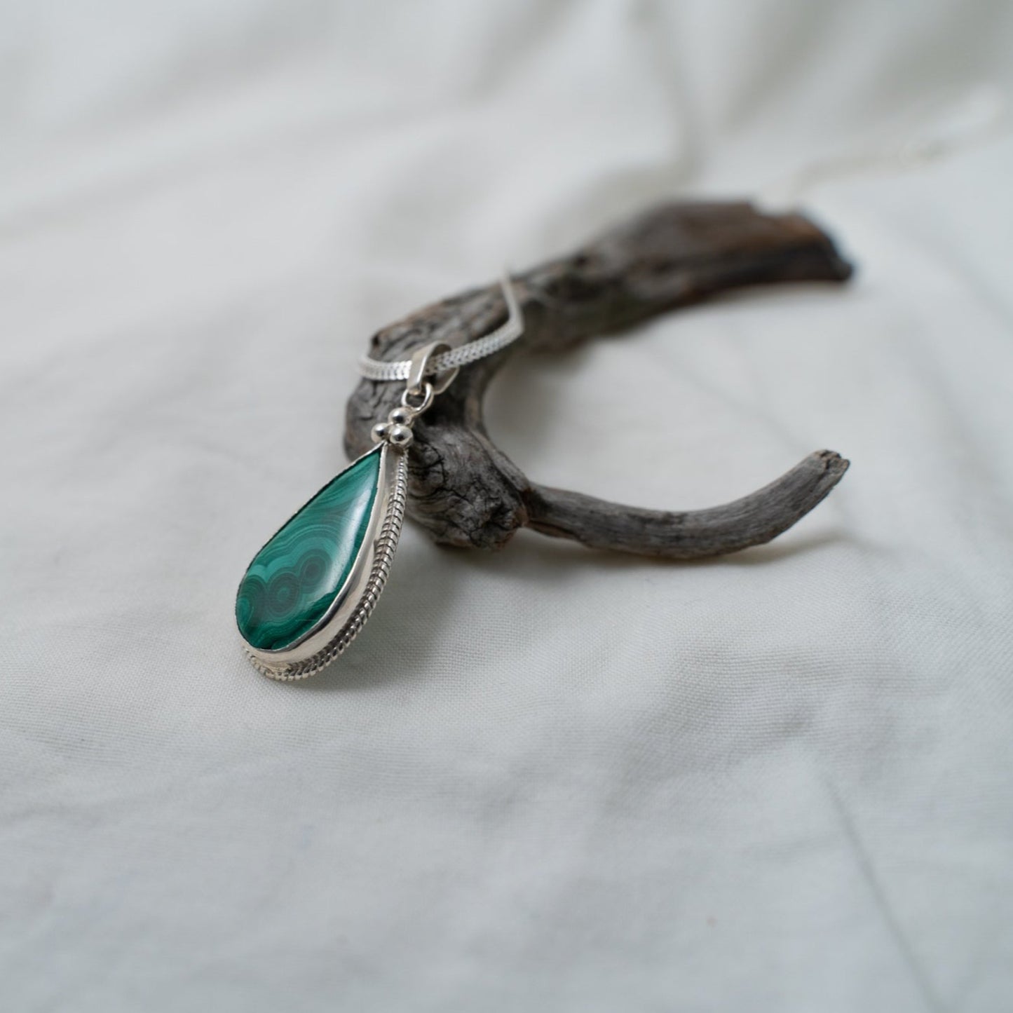A profile shot at an angle to show how this natural, teardrop, malachite, silver pendant would look from different views.