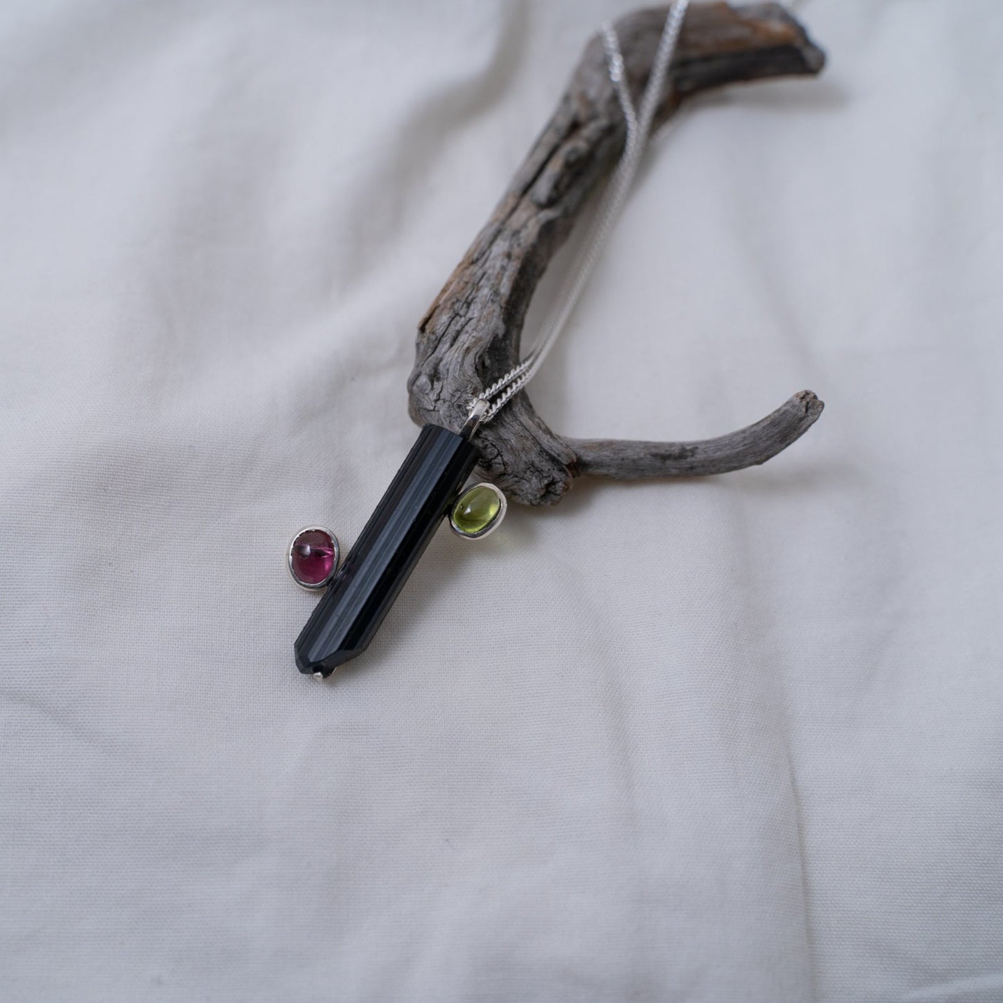 A side shot of the black and pink tourmaline with a green peridot silver pendant. It shows a different angle of how you would see the pendant from the side.