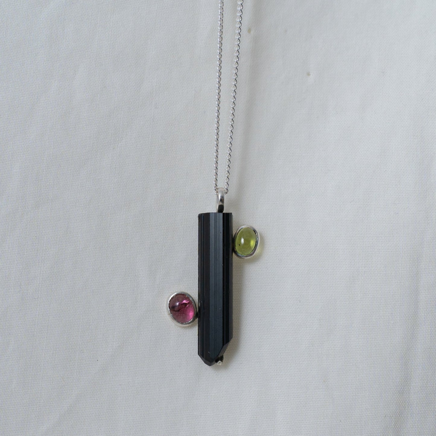 A head on photograph of the black and pink tourmaline with a green peridot silver pendant.. It shows you how it would look when worn.