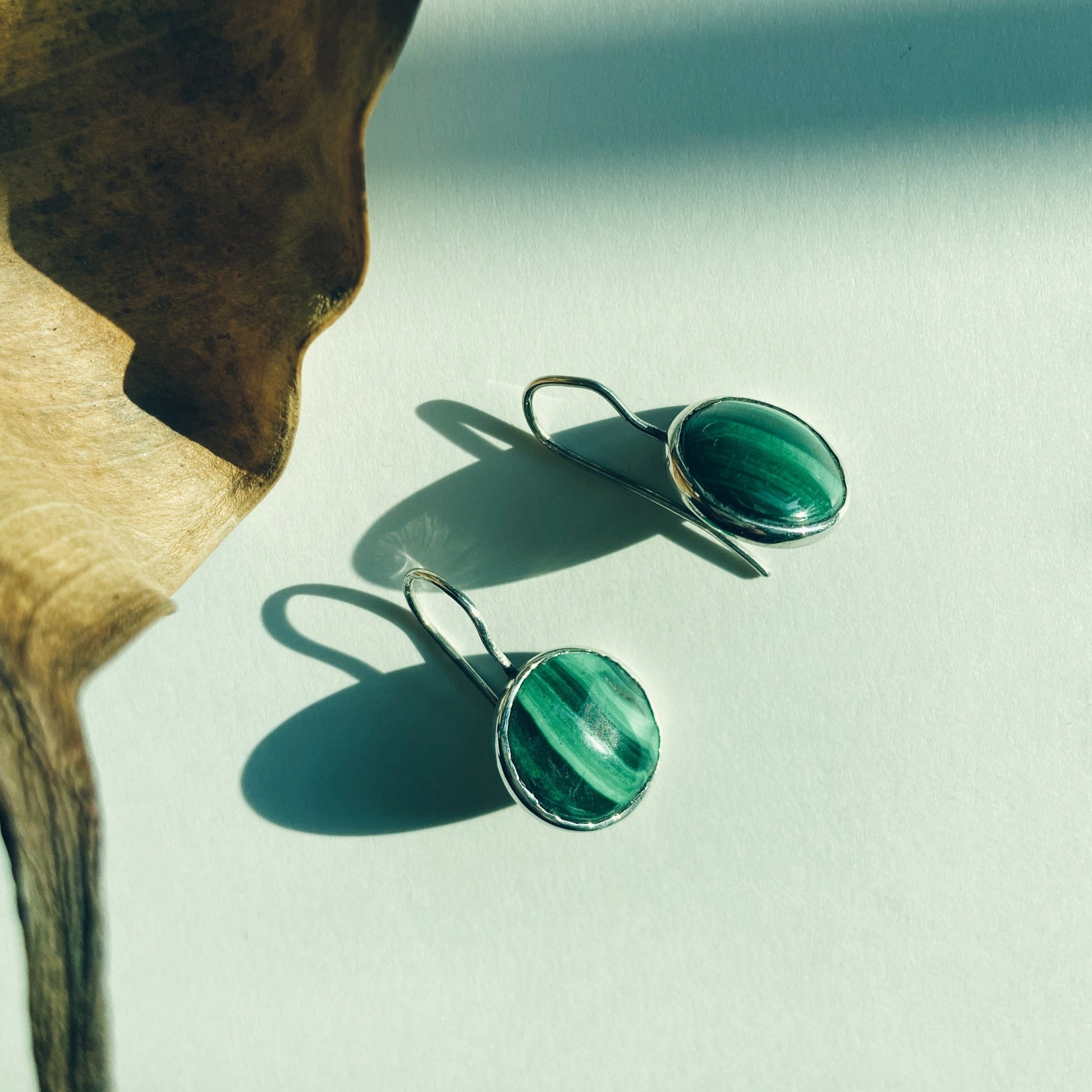 A picture showing a pair of round cabochon, malachite, silver dangle earrings.