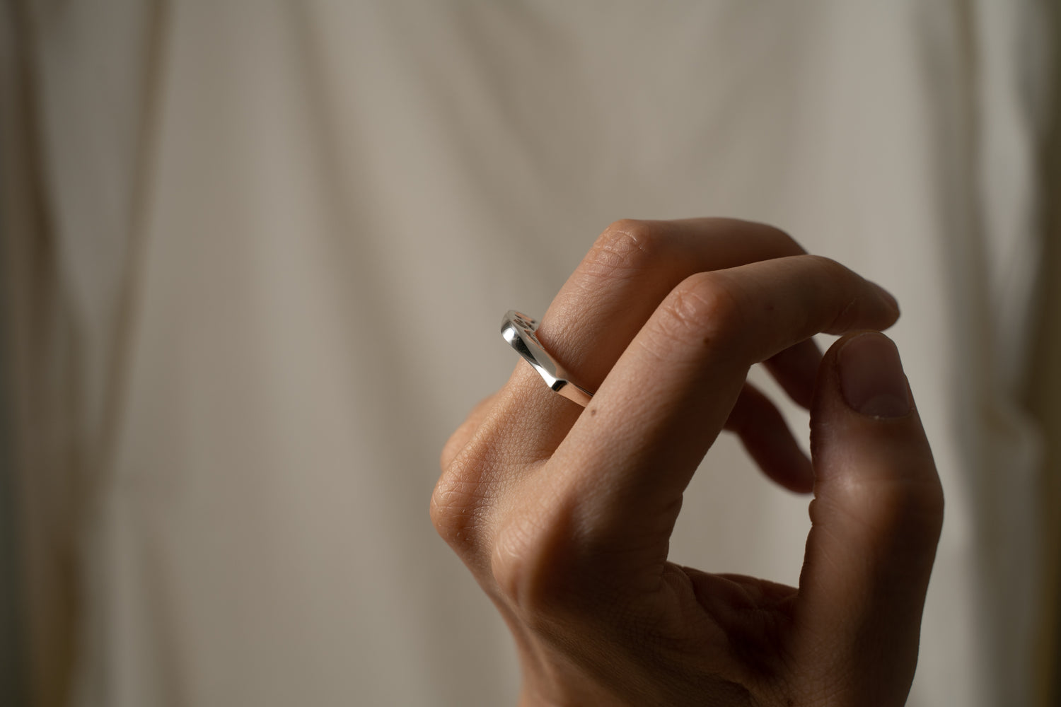 An image of a hand wearing a contemporary design of a silver signet ring. 