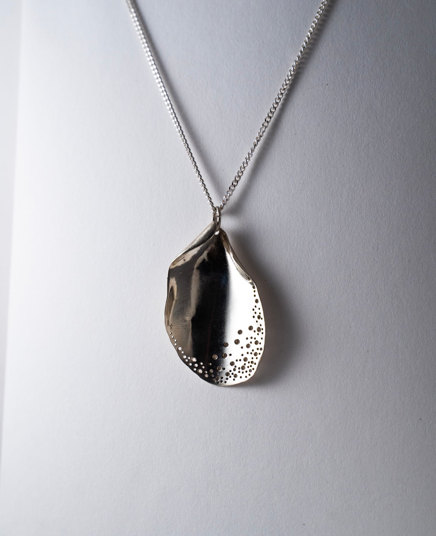 Silver necklace with a textured pendant on a light gray background
