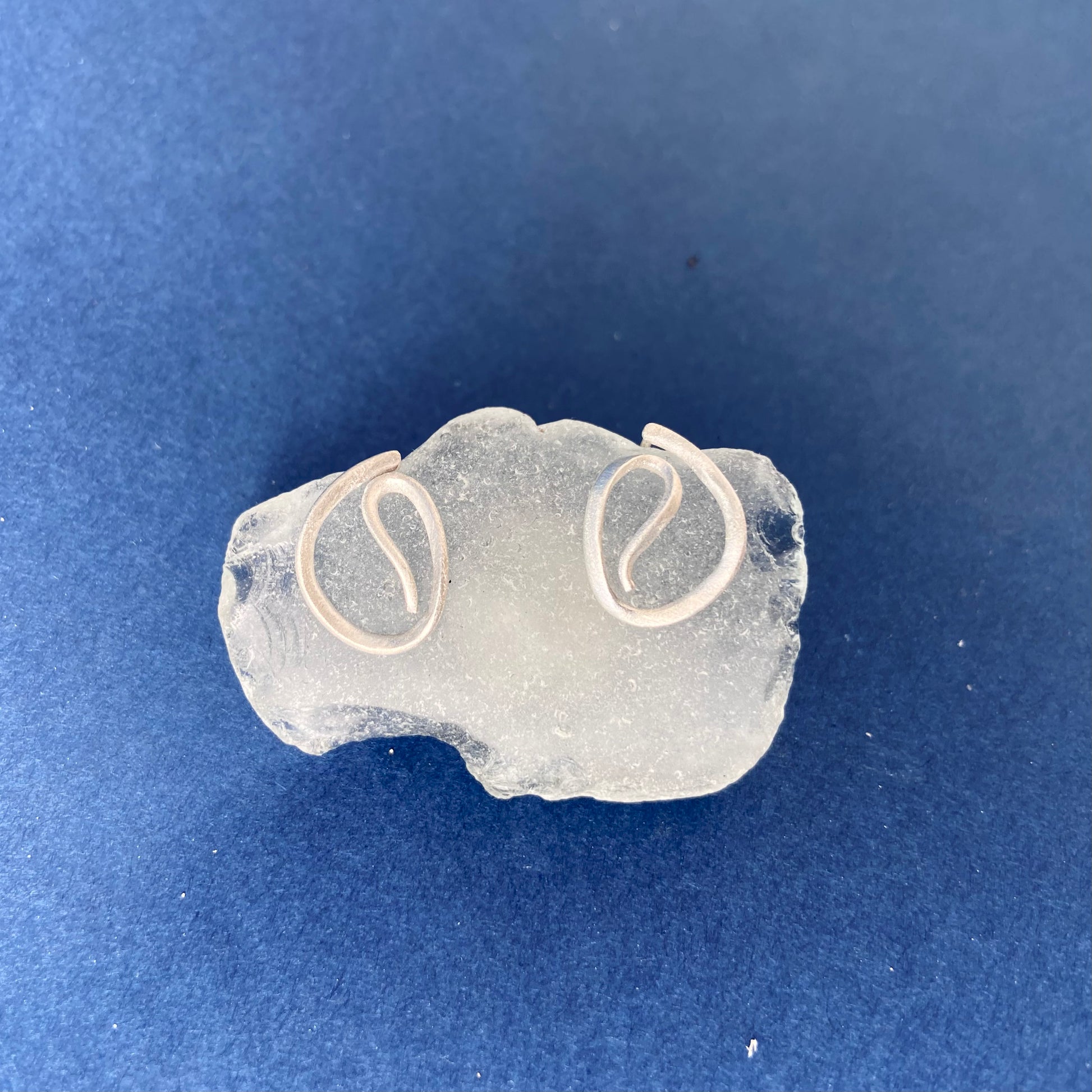 Minimalist artistic earrings for curated ear style, photographed on a piece of glass on a blue background.