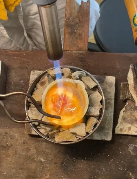 A short clip showing how Anica Lin melts and recycles her gold in her studio. She puts all the pieces she is about to melt into a crucible, add flux to get rid of the impurities and heats it until it is a molten metal ball before pouring it into an ingot mold.