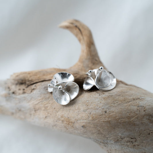 handcrafted floral silver studs photographed on a piece of driftwood. These studs are designed after the bourgainvillea flowers from Southern Africa. A flower that reminds me of home, these delicate pieces are meant to sit on your ear. 
